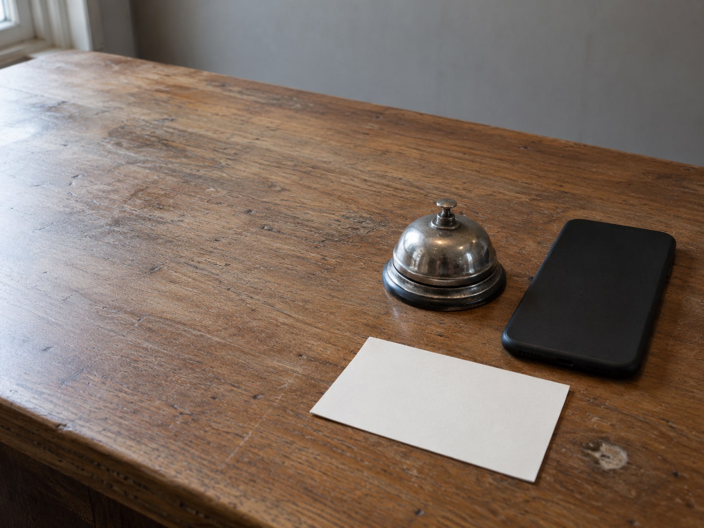 A face-down phone on a service counter beside a small bell and a blank index card.
