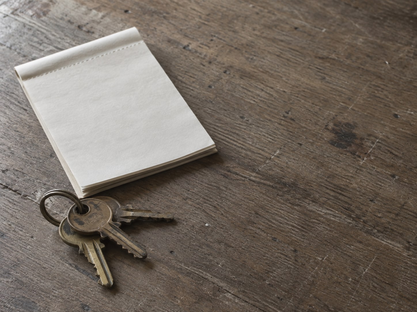 A ring of small brass keys on a wooden desk beside a folded blank invoice pad.