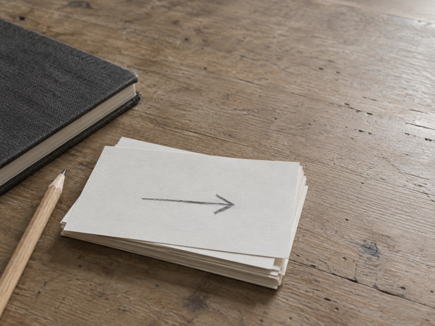 A stack of index cards, one with a hand-drawn arrow, next to a closed notebook and a pencil.