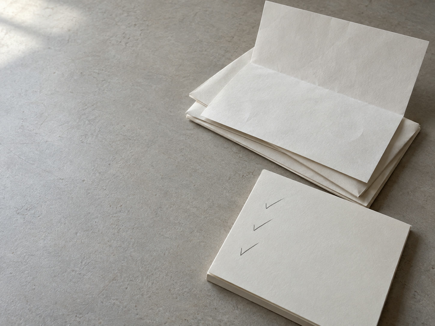 A folded letter resting on a stack of papers beside a pad with three pencil ticks.