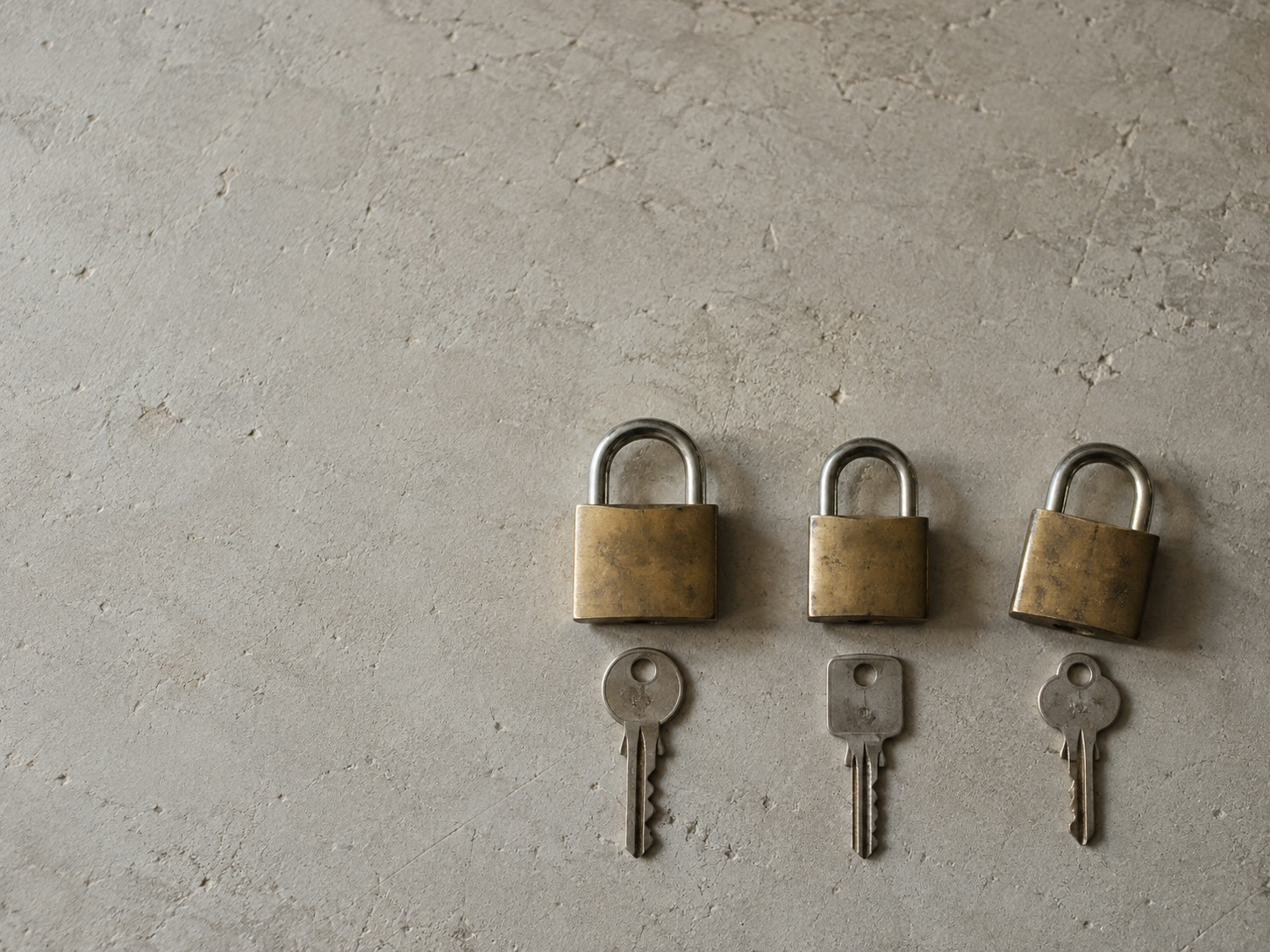 Three different keys laid in a row on a plain surface, each beside its own small lock.