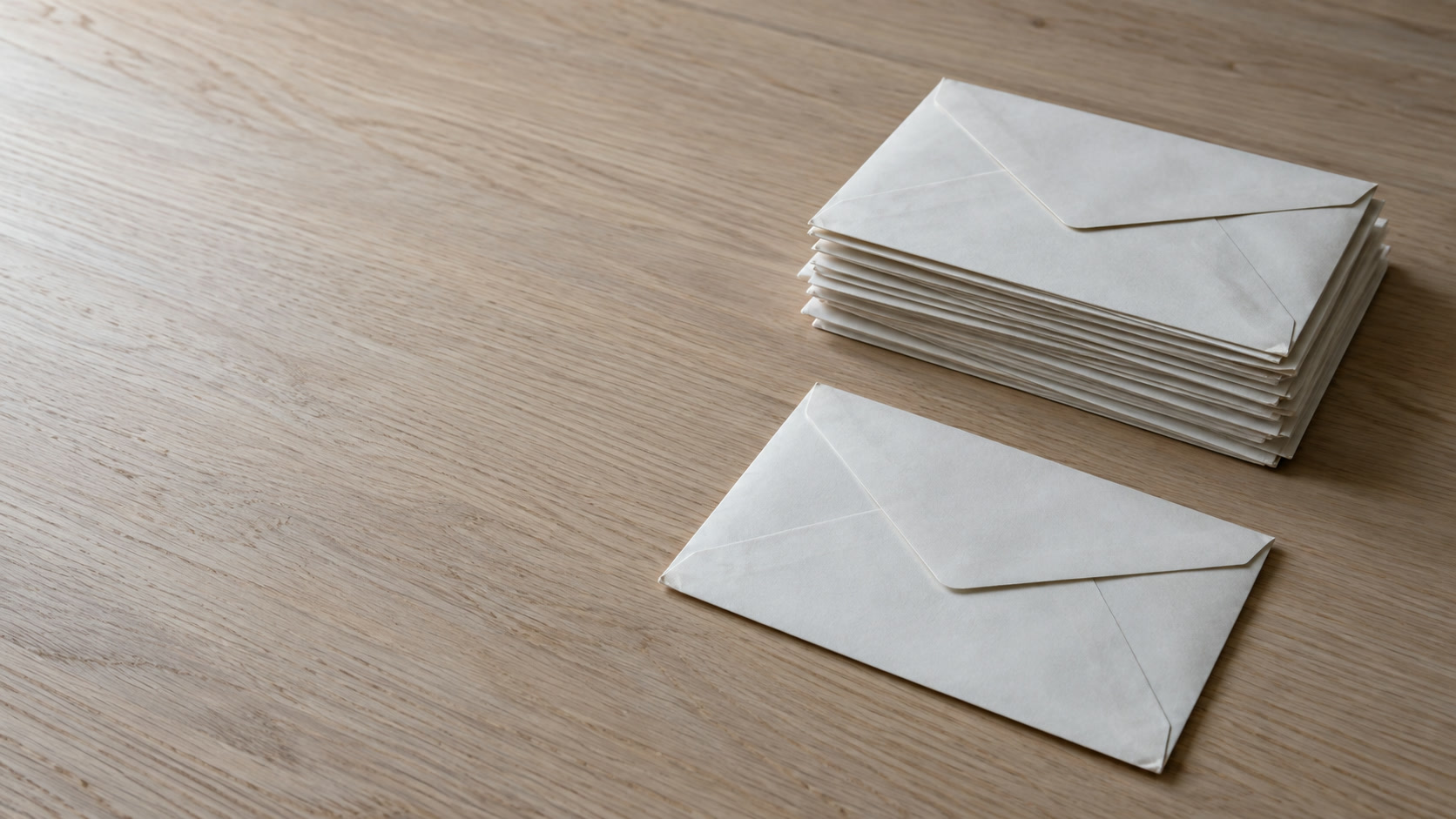 A single envelope set apart from a neat stack of other envelopes on a plain desk.