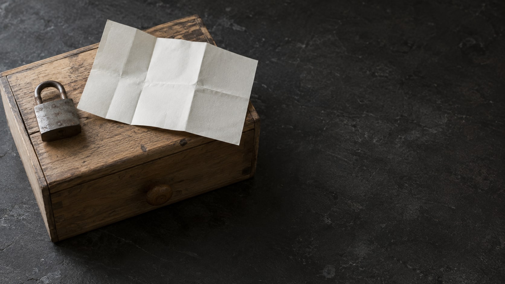 A small padlock resting on a closed wooden drawer beside a folded paper map on a slate desk.