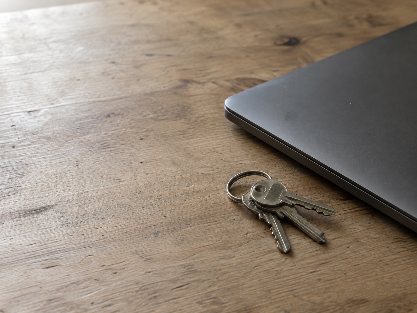 A small ring of keys lying next to a closed laptop on a bare wooden desk.