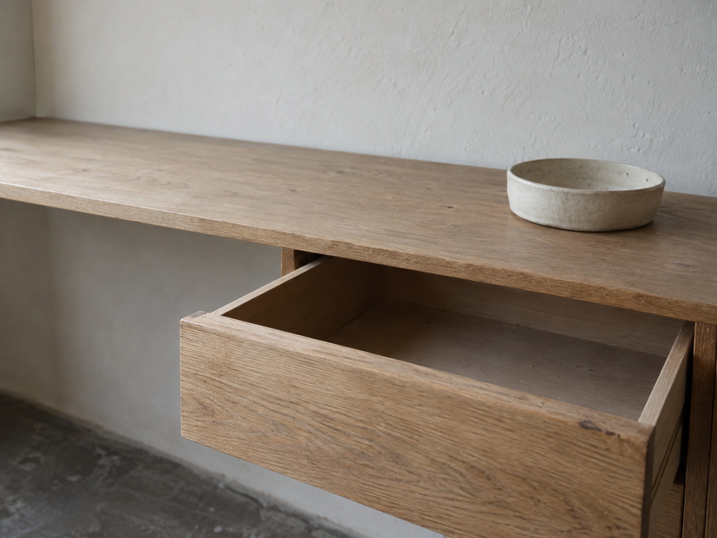 A wooden drawer pulled halfway open with nothing inside, next to a small empty ceramic dish on a shelf.