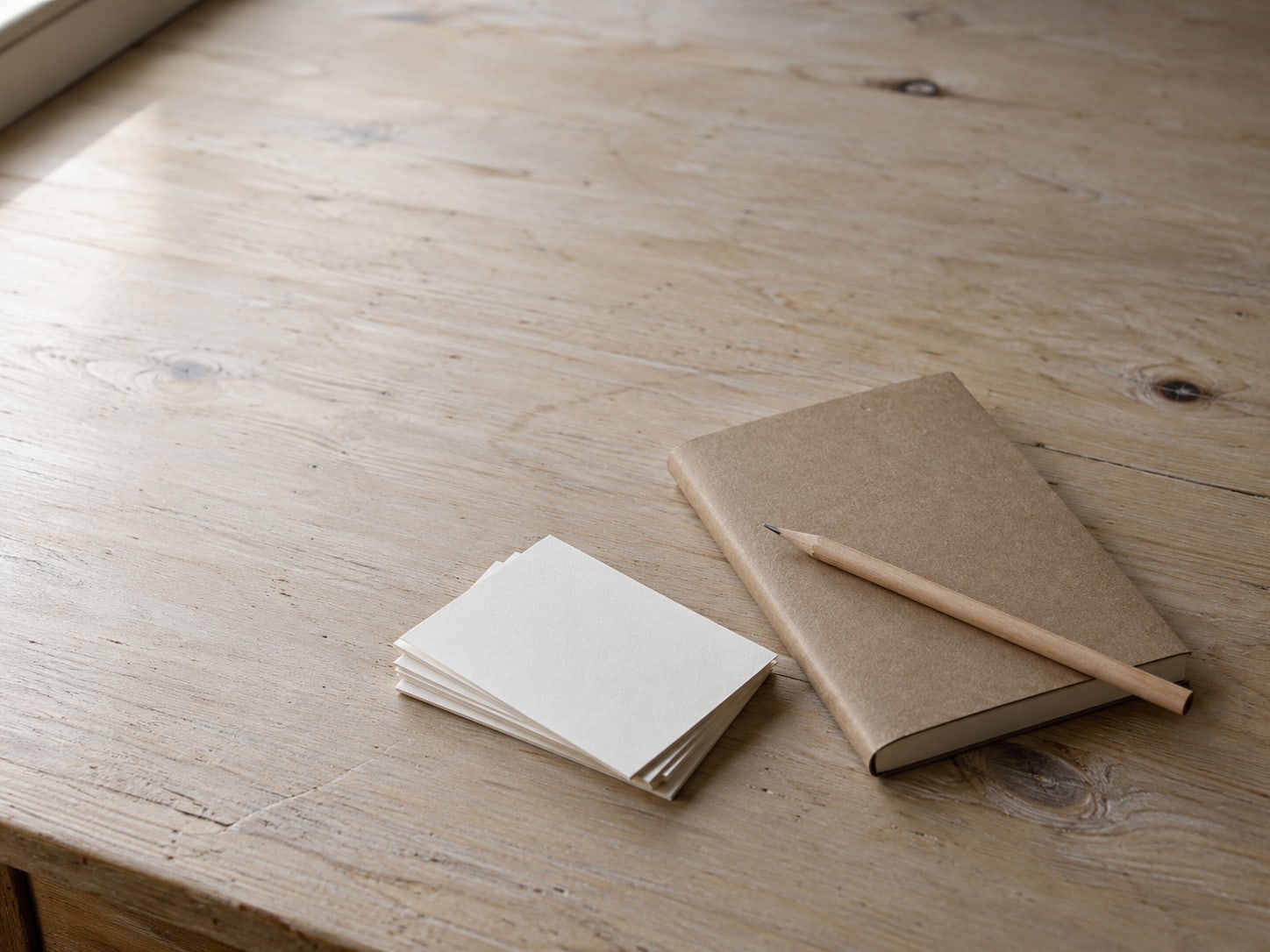 Una libreta cerrada con un lápiz encima, junto a una pequeña pila de tarjetas de índice en blanco.