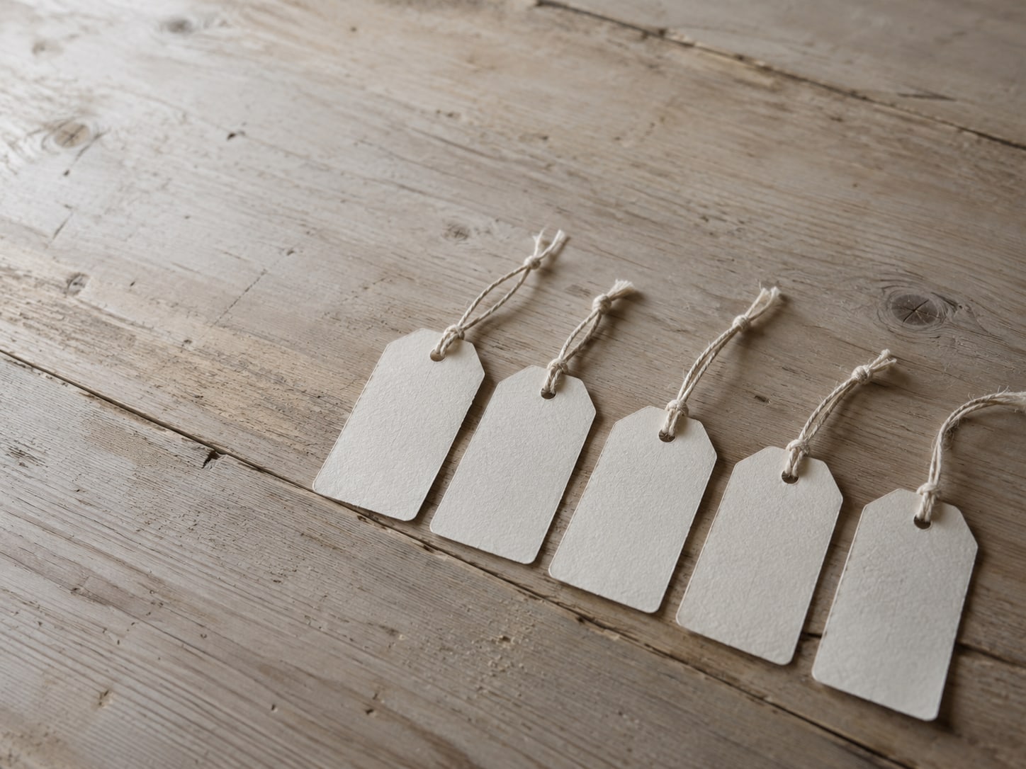 Una fila de etiquetas de papel en blanco atadas con cordel y dispuestas sobre una superficie de madera.