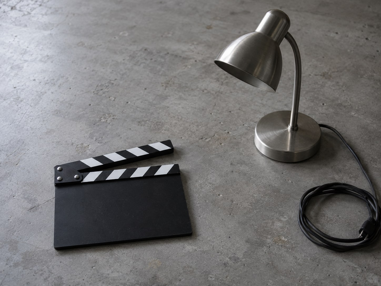 A small desk lamp, a coiled cable and a blank clapperboard resting on a gray tabletop.