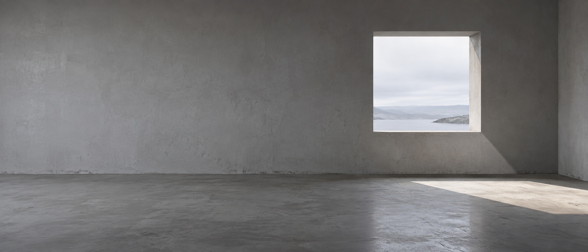 A long plain plastered wall with a single square opening off centre, daylight falling through it onto the floor.