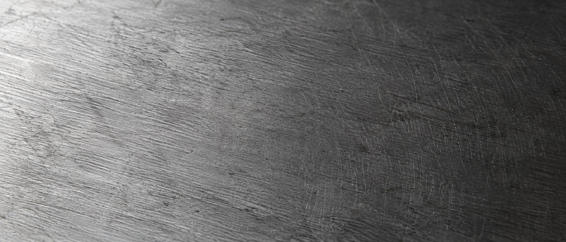 The surface of cold-rolled steel filling the frame, its grain and fine scratches picked out by light crossing at a low angle.