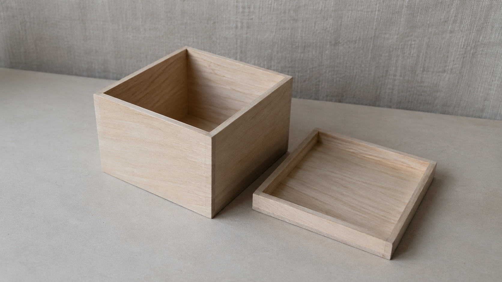 A plain wooden box open on a bare table, its lid set down beside it, nothing inside.